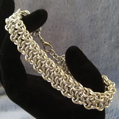 Silver chain mail bracelet stretched between black velvet fingers on a blue background.