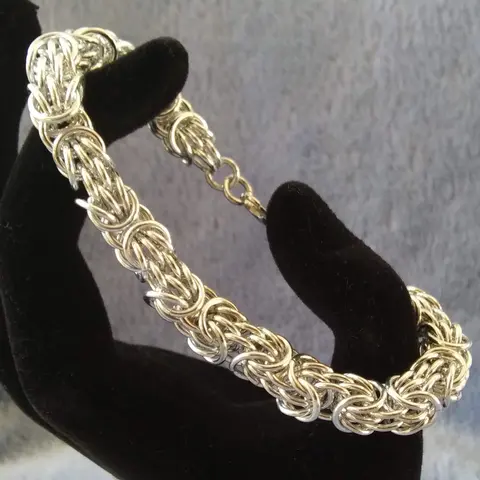 Silver chain mail bracelet stretched between black velvet fingers with a blue background.