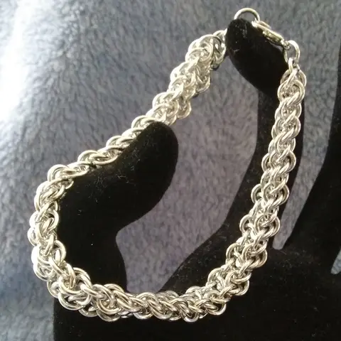 Silver chain mail bracelet stretched between black velvet fingers with a blue background.