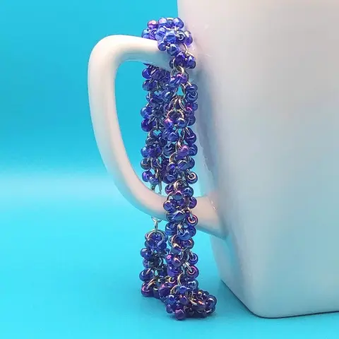 Silver chain mail bracelet with sapphire rainbow beads hanging on a white mug with a blue background