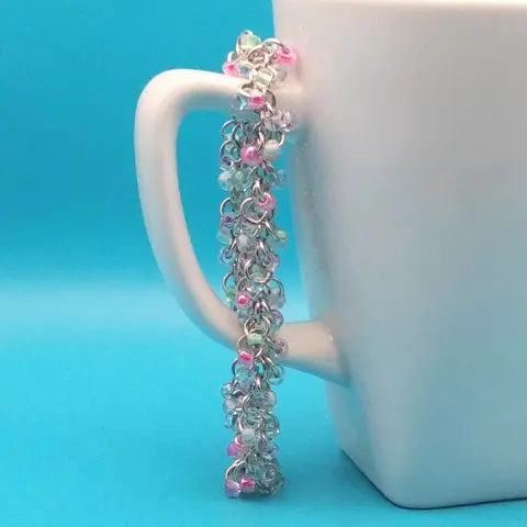 Silver chain mail bracelet with spring garden beads hanging on a white mug with a blue background