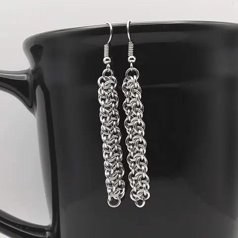 Silver dangly chain mail earrings hanging on a black mug.