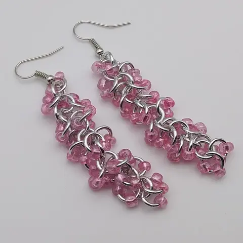 Silver dangly chain mail earrings with pink beads laying on a white background.