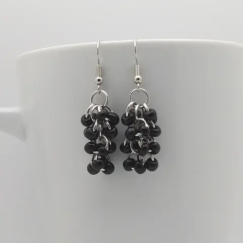 Silver dangly earrings with black beads hanging on a white mug.