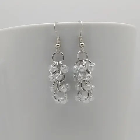 Silver dangly earrings with clear beads hanging on a white mug.