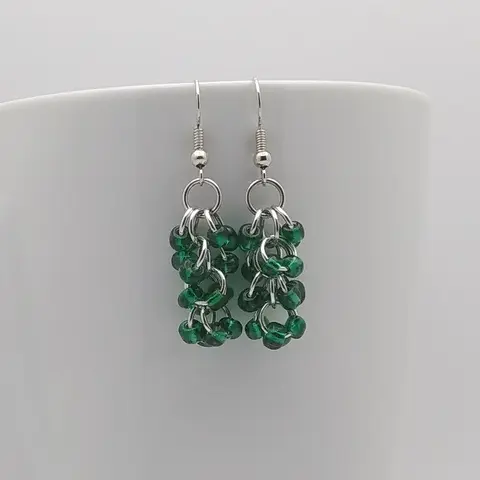 Silver dangly earrings with silver-lined emerald beads hanging on a white mug.