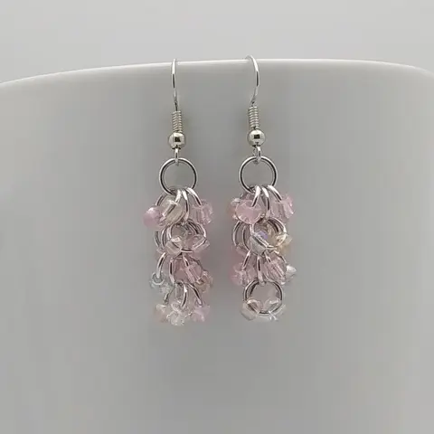 Silver dangly earrings with pink mist beads hanging on a white mug.