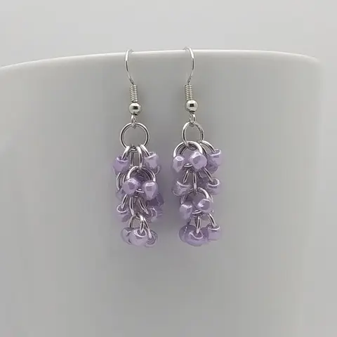 Silver dangly earrings with purple beads hanging on a white mug.