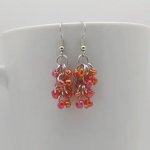 Silver dangly earrings with red rainbow beads hanging on a white mug.