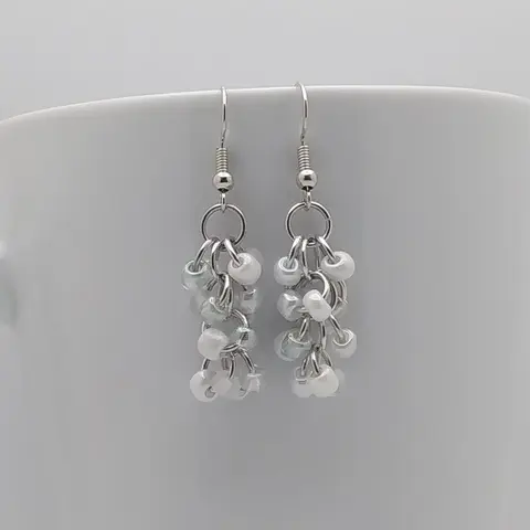 Silver dangly earrings with snow mix beads hanging on a white mug.