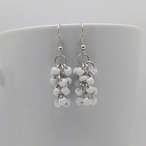 Silver dangly earrings with white beads hanging on a white mug.