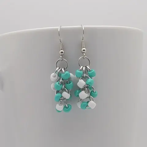 Silver dangly earrings with white and turquoise beads hanging on a white mug.