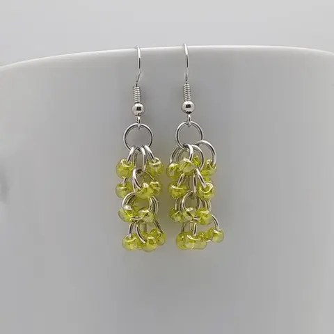 Silver dangly earrings with yellow luster beads hanging on a white mug.