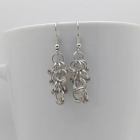 Silver dangly earrings with silver-lined clear beads hanging on a white mug.