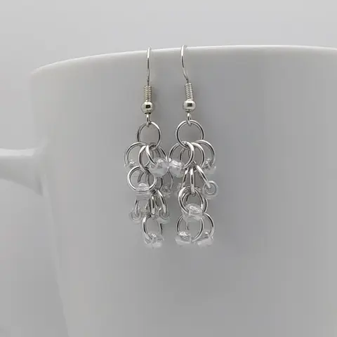 Silver dangly earrings with crystal luster beads hanging on a white mug.