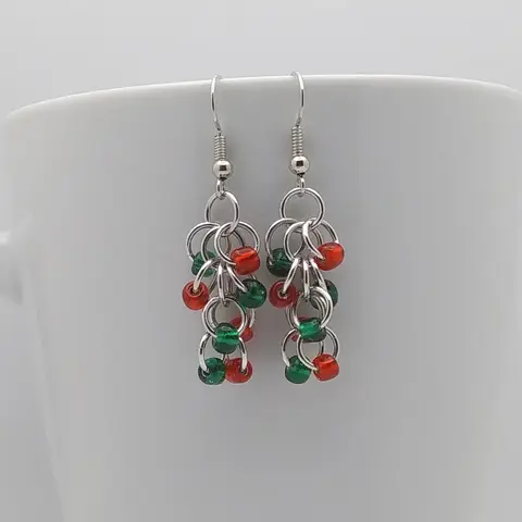 Silver dangly earrings with emerald and red beads hanging on a white mug.