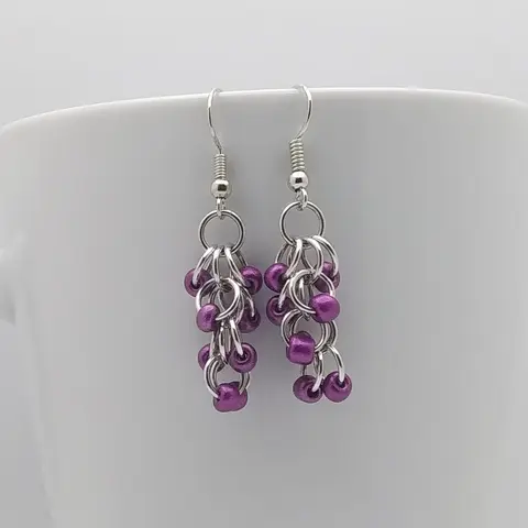 Silver dangly earrings with metallic violet beads hanging on a white mug.