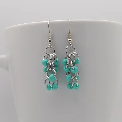 Silver dangly earrings with opaque turquoise beads hanging on a white mug.