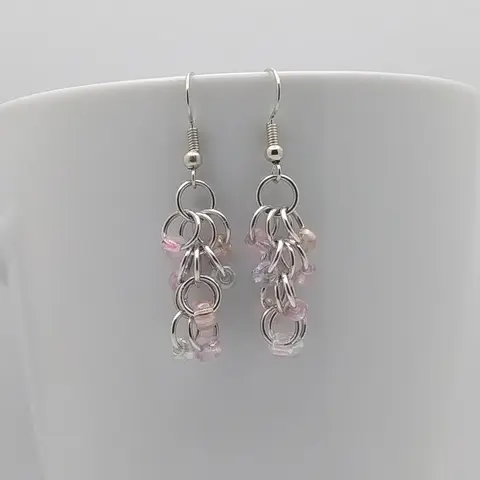 Silver dangly earrings with pink mist beads hanging on a white mug.