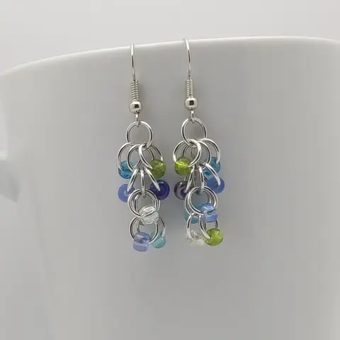 Silver dangly earrings with turquoise mix beads hanging on a white mug.