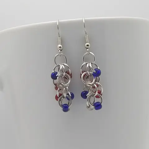 Silver dangly earrings with USA mix beads hanging on a white mug.