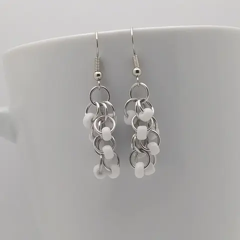 Silver dangly earrings with white beads hanging on a white mug.