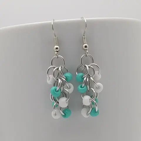 Silver dangly earrings with white and turquoise beads hanging on a white mug.