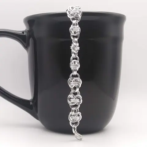 Bright silver aluminum chain mail bracelet on a black mug.