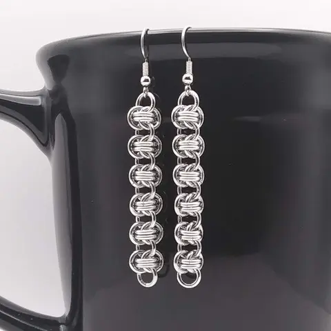 Bright silver aluminum chain mail earrings on a black mug.