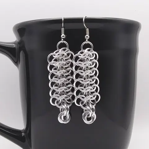 Bright silver aluminum chain mail earrings on a black mug.