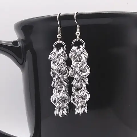 Bright silver aluminum chain mail earrings on a black mug.