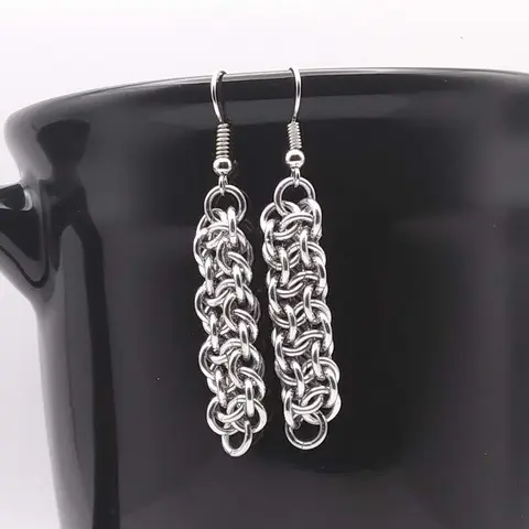 Silver dangly chain mail earrings hanging on a black mug.