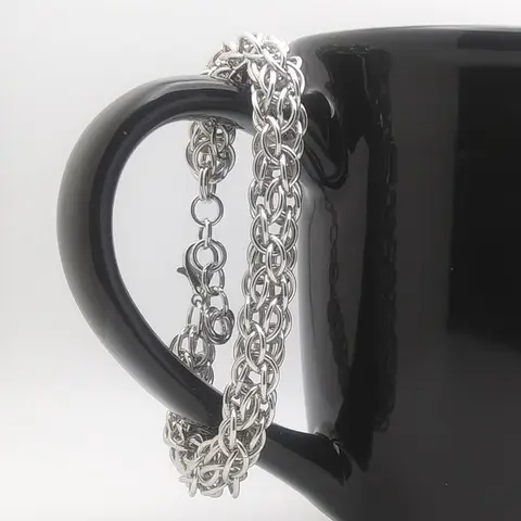 Bright silver aluminum chain mail bracelet hanging on a black mug.