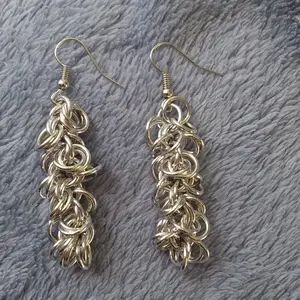 Silver dangly chain mail earrings laying on a blue background.