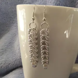 Silver dangly chain mail earrings hanging on a white mug.