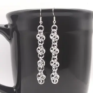 Silver dangly chain mail earrings hanging on a black mug.