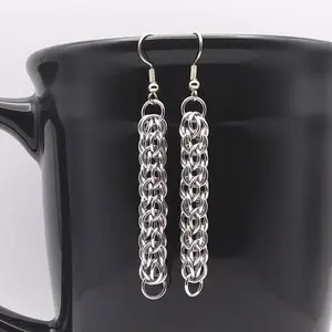 Silver dangly chain mail earrings hanging on a black mug.