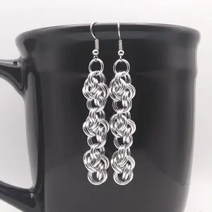 Bright silver aluminum dangly chain mail earrings on a black mug.