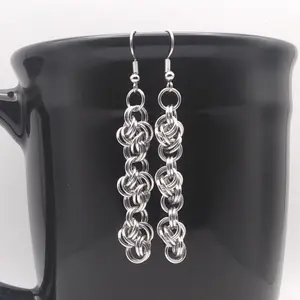 Silver dangly chain mail earrings hanging on a black mug.