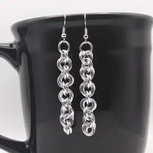 Silver dangly chain mail earrings hanging on a black mug.