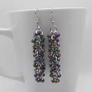 Silver dangly chain mail earrings with dark rainbow beads hanging on a white mug.