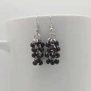 Bright silver aluminum chain mail earrings with black beads on a white mug.