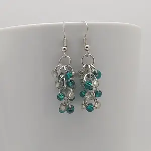 Bright silver aluminum chain mail earrings with clear and teal beads on a white mug.