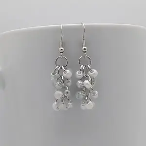 Bright silver aluminum chain mail earrings with snow mix beads on a white mug.