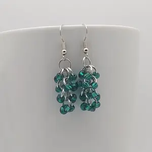 Bright silver aluminum chain mail earrings with silver-lined teal beads on a white mug.