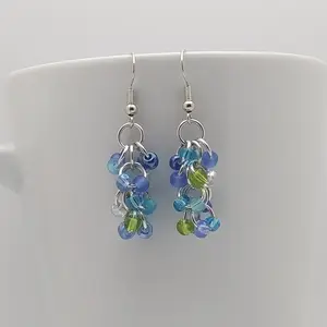 Bright silver aluminum chain mail earrings with turquoise mix beads on a white mug.