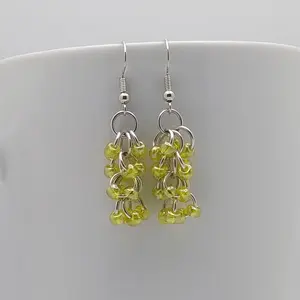 Bright silver aluminum chain mail earrings with yellow luster beads on a white mug.