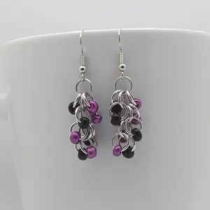 Bright silver aluminum chain mail earrings with black and metallic violet beads on a white mug.