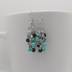 Bright silver aluminum chain mail earrings with black and turquoise beads on a white mug.