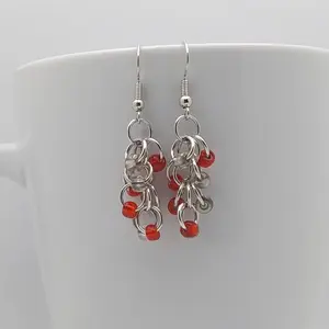 Silver dangly earrings with clear and red beads hanging on a white mug.